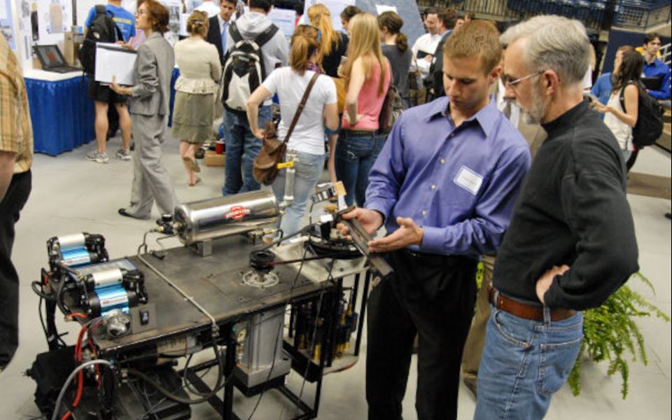Senior Justin Swann (left) talks about his project Air Steam Hybrid Engine at Senior Design Demonstration Day held at Gampel Pavilion.